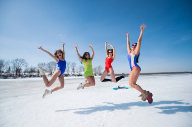Dört beyaz mayo giymiş kadın, karlı bir sahilde oynaşıyorlar. Kış eğlencesi