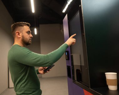 Beyaz adam kahveyi self-servis makinesinden seçiyor.