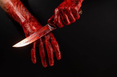 Bir adam kanlı bir bıçağı siyah bir arka planda siliyor.