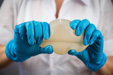 Bir plastik cerrah silikon göğüs implantlarının gücünü onları sıkarak gösterir.