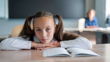 Küçük beyaz kız okuldaki dersten sıkıldı. Liseli kız başını masaya koydu ve öğretmen arka planda oturdu.