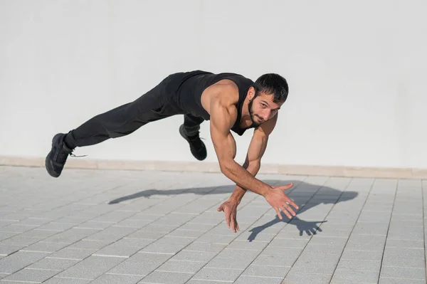 A man in black sportswear jumps while doing push-ups outdoors