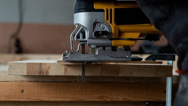 Close-up of a man cutting a wooden plank with an electric jigsaw in a workshop