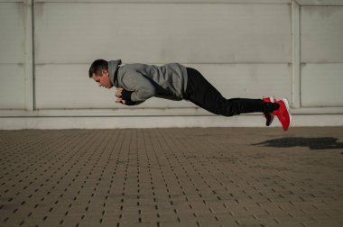 Kapüşonlu bir adam dışarıda şınav çekerken zıplıyor.