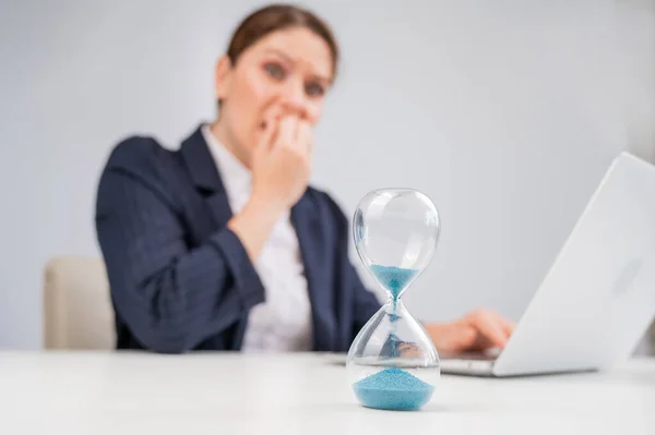Business woman looks at the hourglass with fright. Deadline