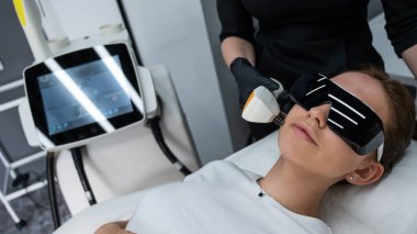 Gözlüklü genç beyaz kadın, fotojenizasyon prosedürü uyguluyor. Güzellik kliniğindeki bir kızın portresi.