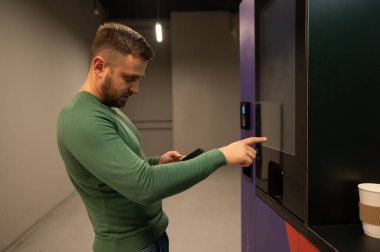 Beyaz adam kahveyi self-servis makinesinden seçiyor.