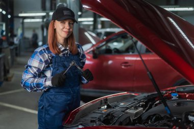 Tulumlu bir kadın tamirci araba tamir ediyor.