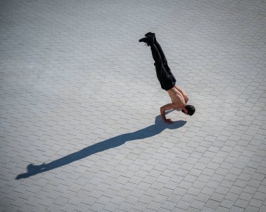 Tişörtsüz bir adam dışarıda elini kolunu sallayarak yürüyor. Yukarıdan görüntüle
