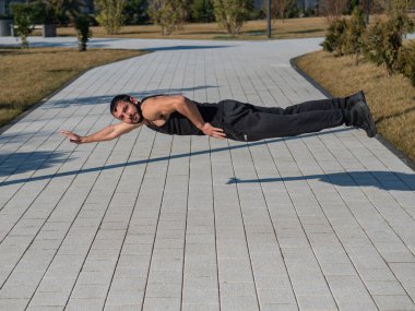 Siyah spor kıyafetli bir adam parkta şınav çekerek zıplıyor.