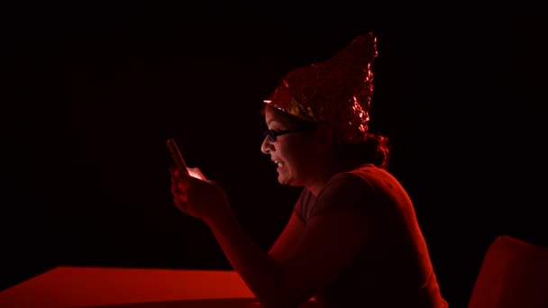 チフォイル帽子をかぶったスマートフォンを使用してパラノイアの原因アジアの女性 陰謀説 — ストック動画