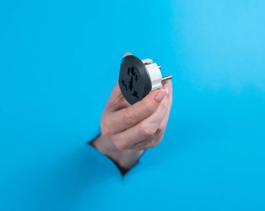 Bir kadın çıkış adaptörü tutuyor. Bir kadın elini mavi bir arka planda bir delikten uzatır.