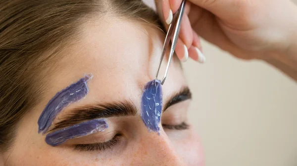 Eyebrow correction. The master removes excess hairs with wax and tweezers