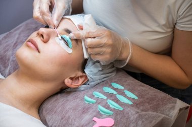 Usta, müşterilerin kirpiklerindeki katman bileşimini pamuklu bezle temizliyor. Kirpik perma prosedürü