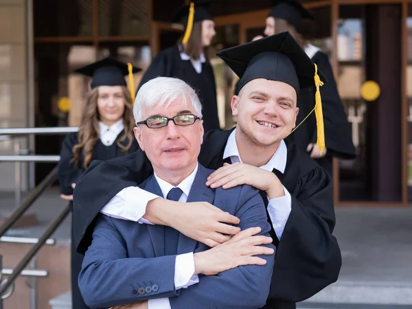 Father and son embrace at graduation. Parent congratulates university graduate