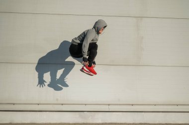 Kapüşonlu beyaz adam elleri dışarıda dizlerinin üzerinde yükseğe zıplıyor.