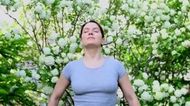 Beyaz kadın parktaki çiçek açan ağaçların kokusundan hoşlanıyor.