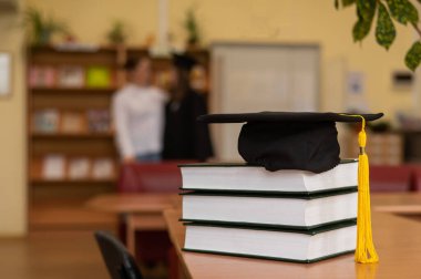 Kütüphanedeki bir yığın kitabın mezuniyet şapkası.