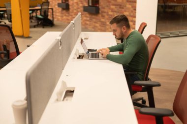 Modern çalışma alanında dizüstü bilgisayarda çalışan beyaz sakallı bir adam.