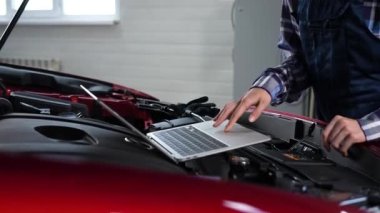 Kadın oto tamircisi dizüstü bilgisayar kullanarak motor kontrolü yapıyor.