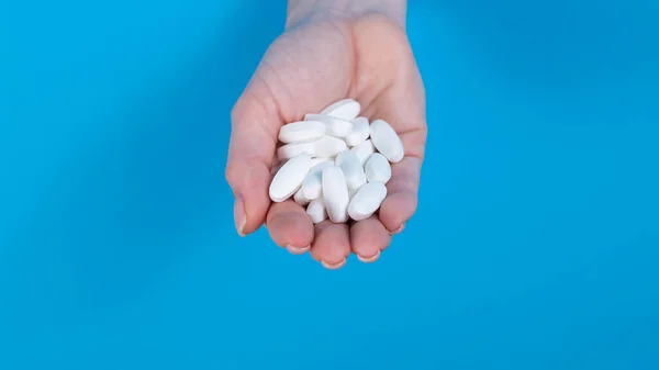 A woman is holding a handful of pills. A womans hand sticks out of a hole in a cardboard blue background