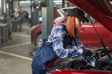 Tulumlu bir kadın tamirci araba tamir ediyor.