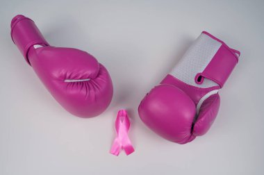 Pembe boks eldivenleri ve beyaz arka planda pembe ipek bir kurdele. Göğüs kanseri kavramı