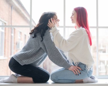 Kazak giymiş iki kadın pencerenin kenarında oturur ve nazikçe sarılırlar. Lezbiyen samimiyeti