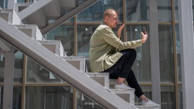 Genç adam merdivenlerde oturup dışarıdaki akıllı telefondan işaret diliyle konuşuyor.