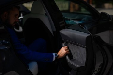 Mavi takım elbiseli bir adam arabanın kapısını açar. Pahalı bir saati olan bir adamın eli.