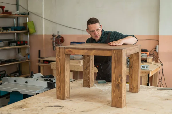 Male carpenter finishing work on wooden table in workshop