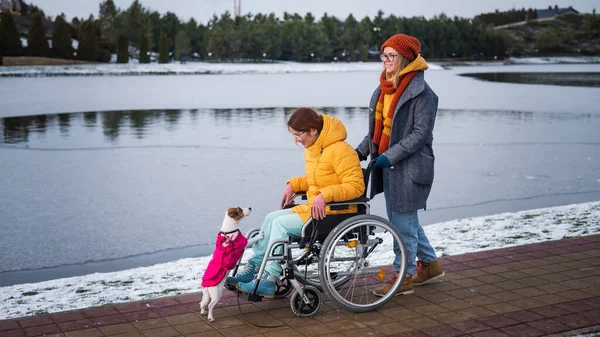 Caucasian woman driving her friend in a wheelchair along the lake in winter
