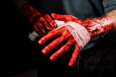 Kanla kaplı bir adam ellerini bandajlıyor.
