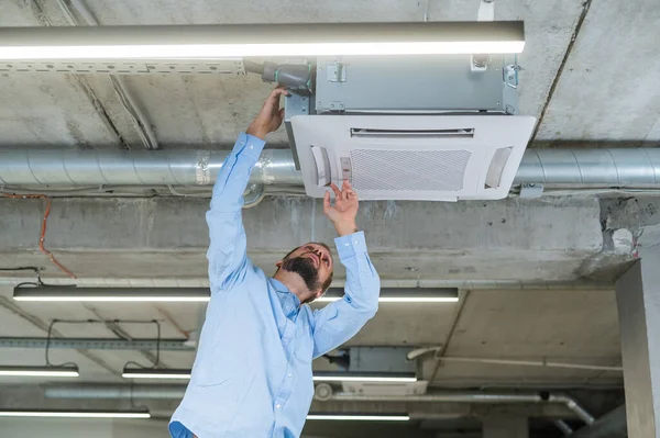 Caucasian bearded man repairing the air conditioner in the office