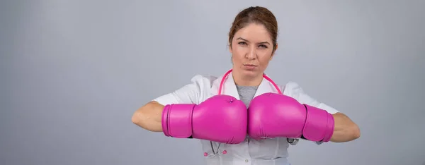 Female doctor in pink boxing gloves with a pink ribbon on a gray background. Fight against breast cancer. Widescreen