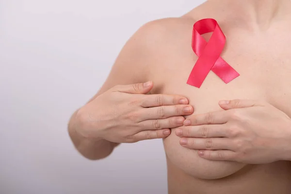 Caucasian woman self-checks for breast cancer. Pink satin ribbon