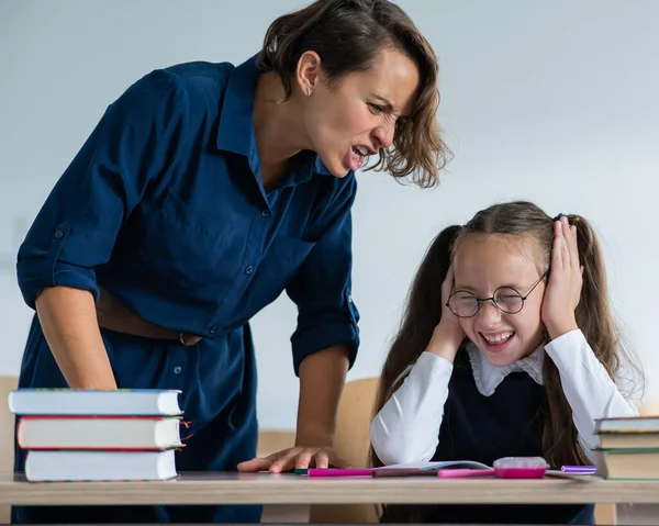 A female teacher yells at a student. Little girl covers her ears with her hands