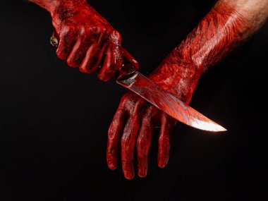 Bir adam kanlı bir bıçağı siyah bir arka planda siliyor.