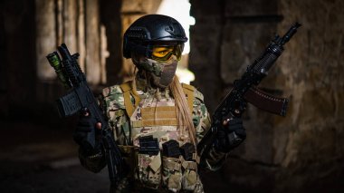 Askeri üniformalı bir kadın terk edilmiş bir binada silah tutuyor.