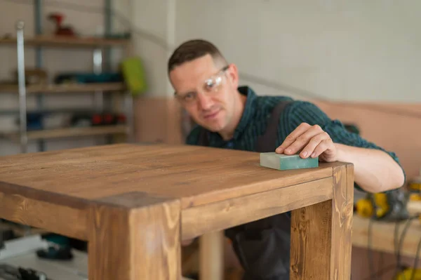 Male carpenter finishing work on wooden table in workshop