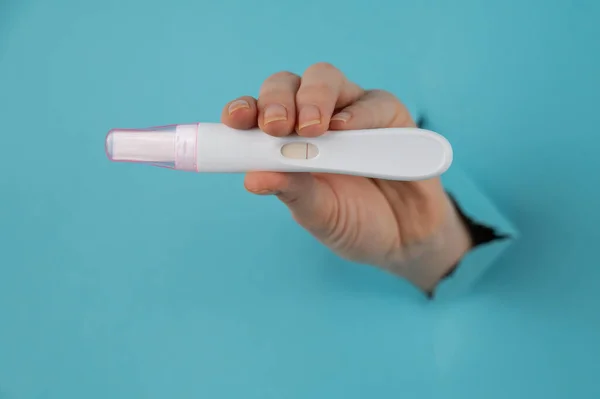 A hand with a negative pregnancy test sticking out of a hole in a blue cardboard background