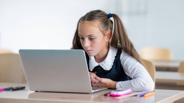 Beyaz kız sınıfta dizüstü bilgisayarla ders çalışıyor.