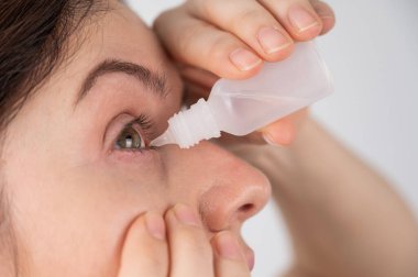 Beyaz kadın gözlerine nemlendirici damlalar damlatıyor