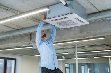 Beyaz sakallı adam ofisteki klimayı tamir ediyor.