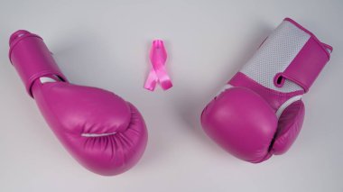 Pembe boks eldivenleri ve beyaz arka planda pembe ipek bir kurdele. Göğüs kanseri kavramı