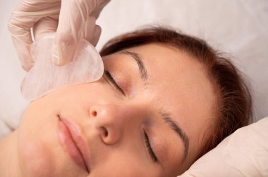 Bir kozmetikçi, müşterinin yüzüne gouache kazıyıcı kullanır.