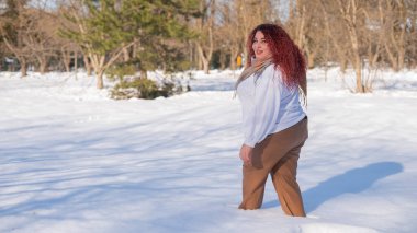 A fat red-haired woman in a white sweatshirt walks through snowdrifts