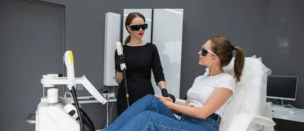 A woman on a couch in goggles undergoing a photorejuvenation procedure. Cosmetologist with a patient