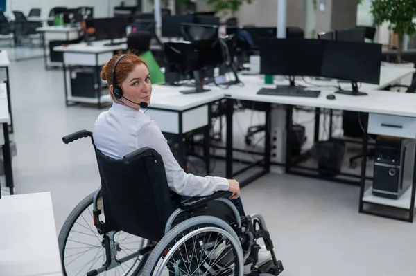Caucasian woman moves around the office in a wheelchair. Female call center worker.