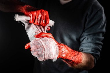 Kanla kaplı bir adam ellerini bandajlıyor.